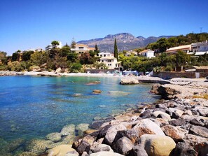 A coastal area with clear waters, rocky shoreline, and buildings with balconies overlooking the sea. - Panos & Antzy  Apartments (Akrogiali)