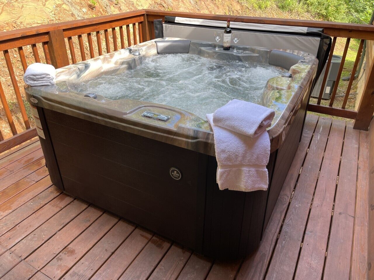 A hot tub on a wooden deck with a control panel and a bottle of wine.