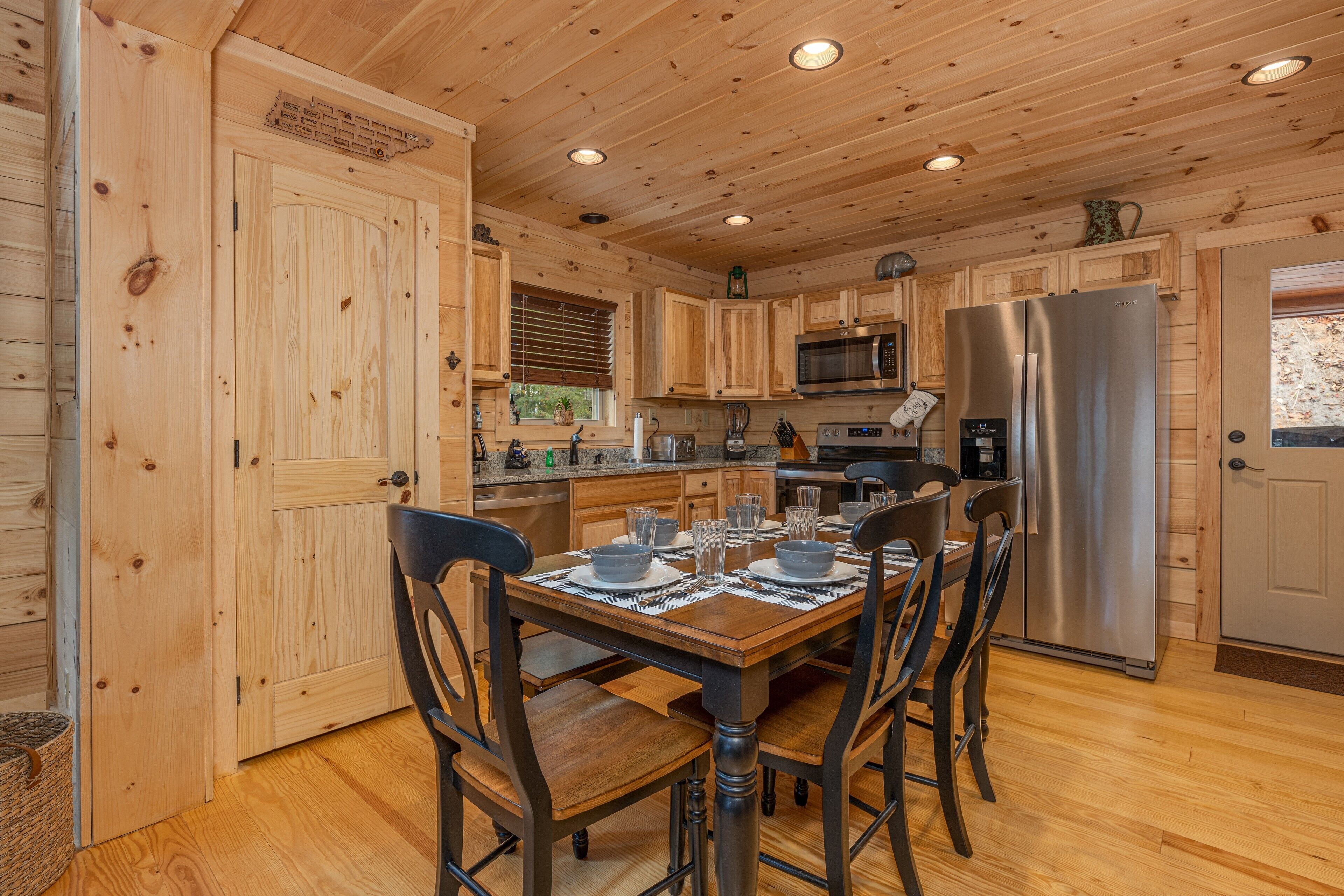 A wooden cabin-style kitchen with a dining table set for four, equipped with a refrigerator, microwave, and various appliances.