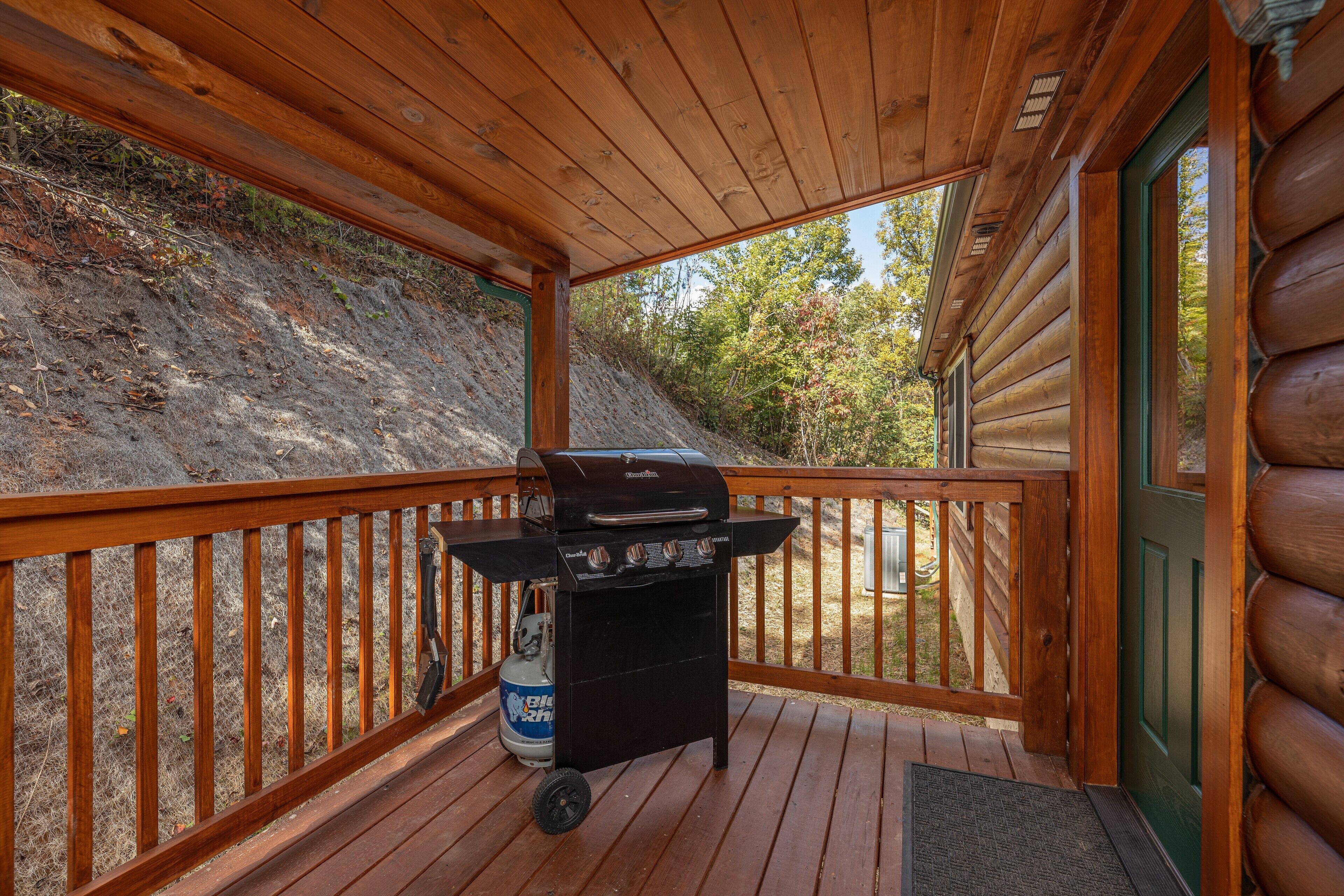 A wooden deck with a barbecue grill and propane tank.