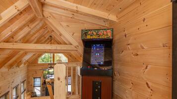 L’intérieur d’un chalet en bois, avec un plafond en bois, un escalier en bois et une borne d’arcade en bois.