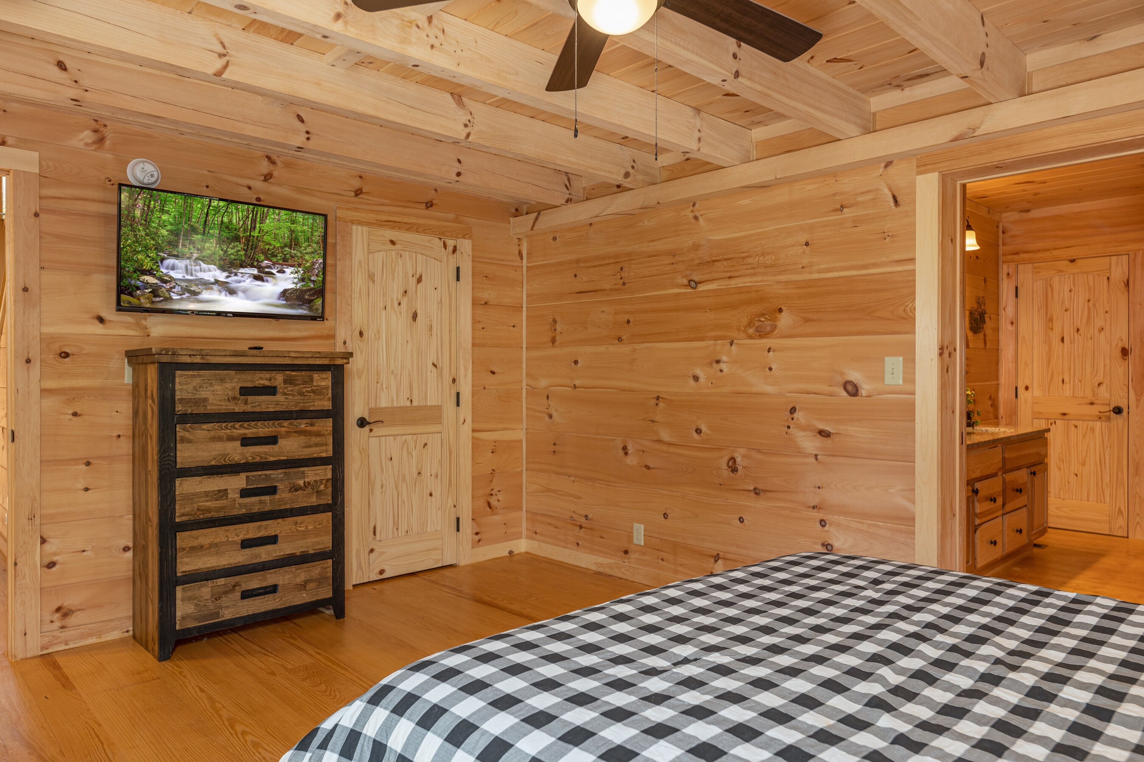L’intérieur d’une cabane en bois, avec un lit, une commode, un téléviseur et un ventilateur de plafond.