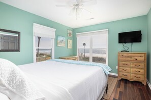 Une chambre à coucher avec un lit, une commode, un téléviseur et une vue sur la plage.