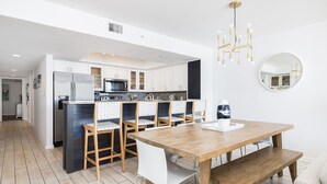 Une cuisine moderne avec des meubles blancs, une table à manger en bois et un lustre.