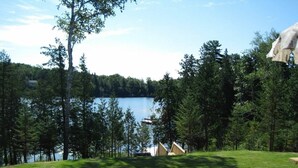 A lakeside view with a paved deck, a stone wall, and a row of cabins. - Welcome to the Chalets du Lac Grenier (Chertsey)