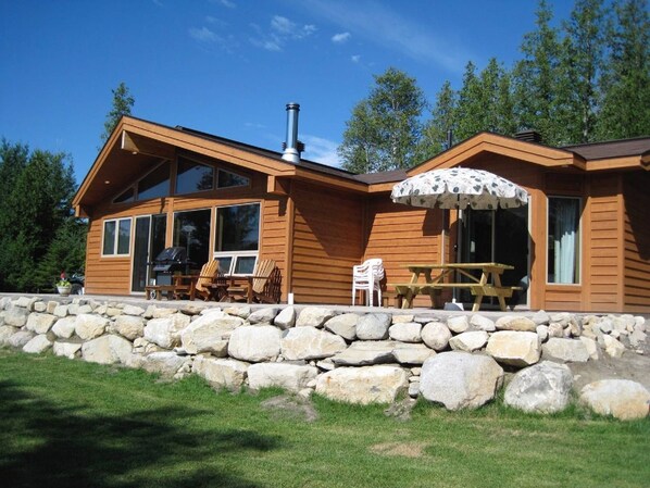 A wooden cabin with a stone foundation, large windows, and outdoor seating.