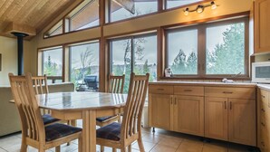A kitchen with wooden cabinets, a dining table with chairs, and large windows offering a view of the outdoors. - Welcome to the Chalets du Lac Grenier (Chertsey)