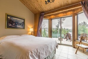 A bedroom with a large bed, a painting, a lamp, and a view of the outdoors through a sliding glass door.