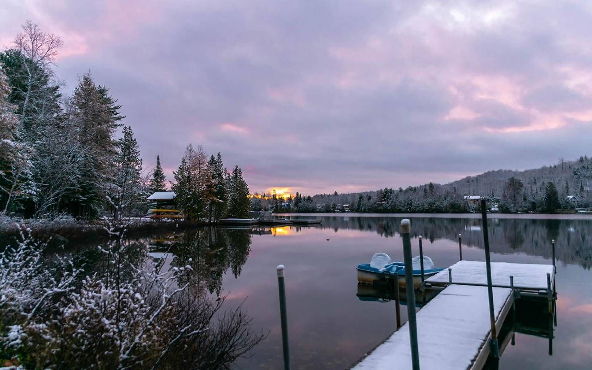 Une scène paisible au bord d’un lac, avec un quai, un bateau à rames et un bâtiment en arrière-plan.