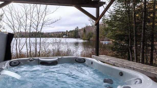 A hot tub with a wooden deck and a lake view.