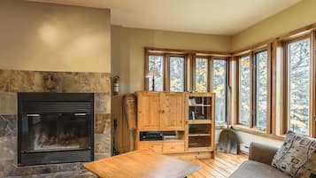 Un salon chaleureux avec une cheminée en pierre, des meubles en bois et de grandes fenêtres donnant sur le paysage automnal aux couleurs flamboyantes.