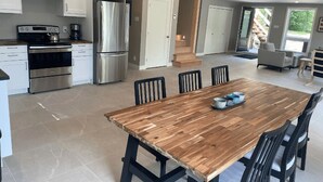 A modern kitchen with stainless steel appliances, a wooden dining table, and a view of the outdoors.