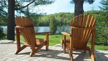 Zwei Adirondack-Stühle mit Blick auf einen See, im Hintergrund ein Wald.