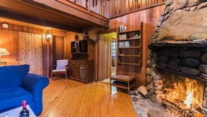 Una habitación acogedora con paredes de madera, una chimenea de piedra, un sofá azul y una estantería.