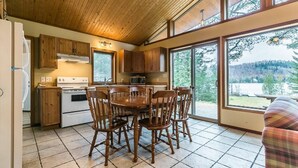 Une cuisine avec des meubles en bois, une table à manger avec des chaises et de grandes fenêtres donnant sur une zone boisée.