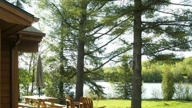 Une terrasse en bois avec des tables et des chaises pour pique-niquer, donnant sur un lac et entourée d’arbres.
