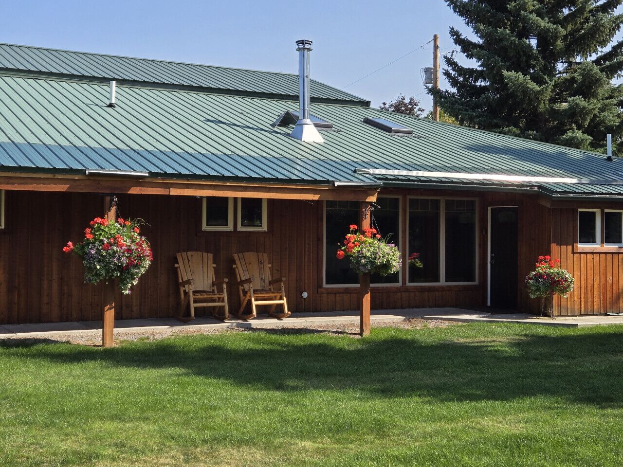 A wooden cabin with a metal roof, two rocking chairs, and flower baskets.