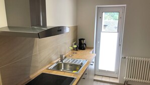 A modern kitchen with a stainless steel range hood, a double sink, and a built-in induction cooktop. There is a coffee maker and a glass on the countertop. - Landhaus Büttner Altenberg (Altenberg)