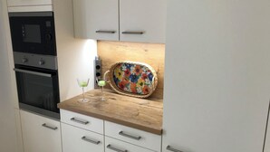 A kitchen with white cabinets, a microwave, an oven, and a wooden countertop with a colorful floral tray. - Landhaus Büttner Altenberg (Altenberg)