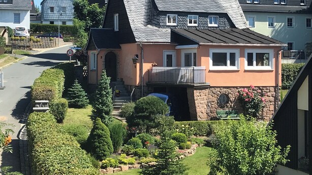 A two-story house with a stone foundation, a balcony, and a garden with various plants and a small pond. - Landhaus Büttner Altenberg (Altenberg)