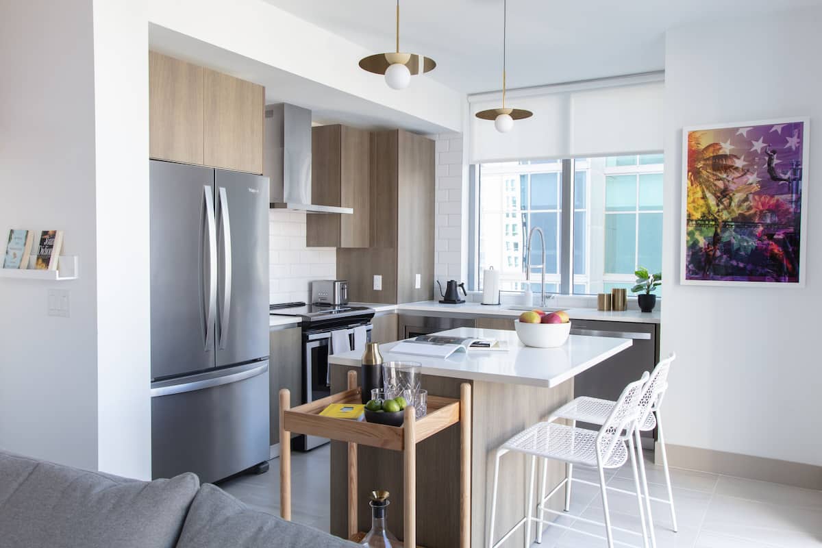 A modern kitchen with a stainless steel refrigerator, wooden cabinets, and a central island with bar stools.