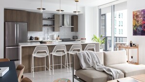 A modern kitchen with a central island, bar stools, and a dining area with a sofa and table. - Mint House Miami - Downtown (Miami)