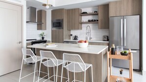 A modern kitchen with a central island, bar stools, stainless steel appliances, and wooden cabinetry. - Mint House Miami - Downtown (Miami)