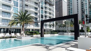 A modern hotel pool area with clear blue water, white lounge chairs, and a palm tree. - Mint House Miami - Downtown (Miami)