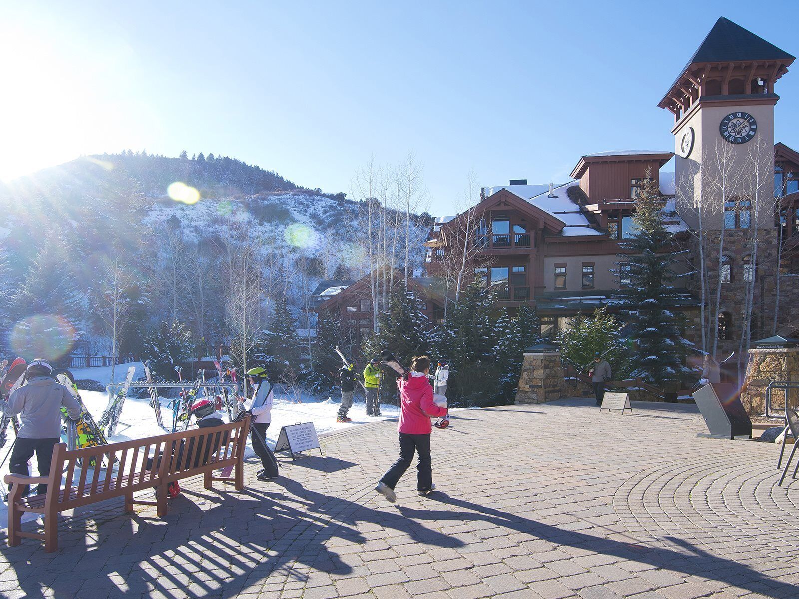 A snow-covered plaza with a clock tower, benches, and buildings in the background.