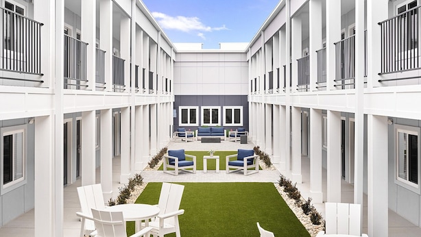 Un patio moderno con mobiliario blanco, un área de estar central y un pequeño césped.