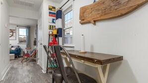 A hallway with a wooden table and chairs, a window with curtains, and a wall-mounted wooden board. - 303 Massachusetts - Adorable one bedroom cottage close to the beach! (Lewes)