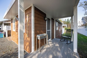 A wooden deck with a rocking chair and a small table, surrounded by a white fence and a grassy yard. - 303 Massachusetts - Adorable one bedroom cottage close to the beach! (Lewes)