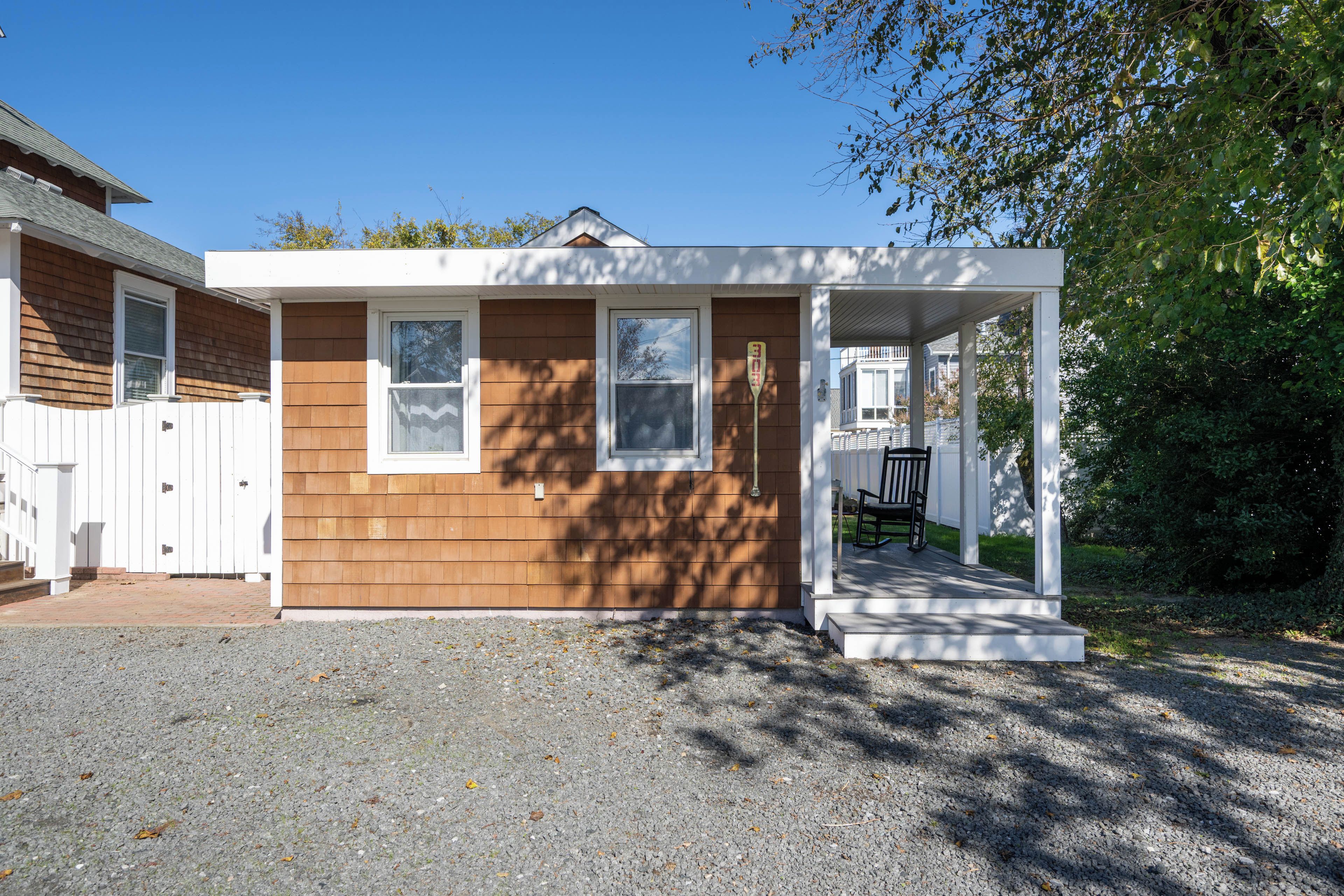 A small wooden cabin with a porch, a fenced yard, and a clear sky.