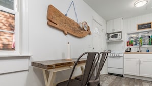 A kitchen with white cabinets, a wooden table, and a brown chair. - 303 Massachusetts - Adorable one bedroom cottage close to the beach! (Lewes)
