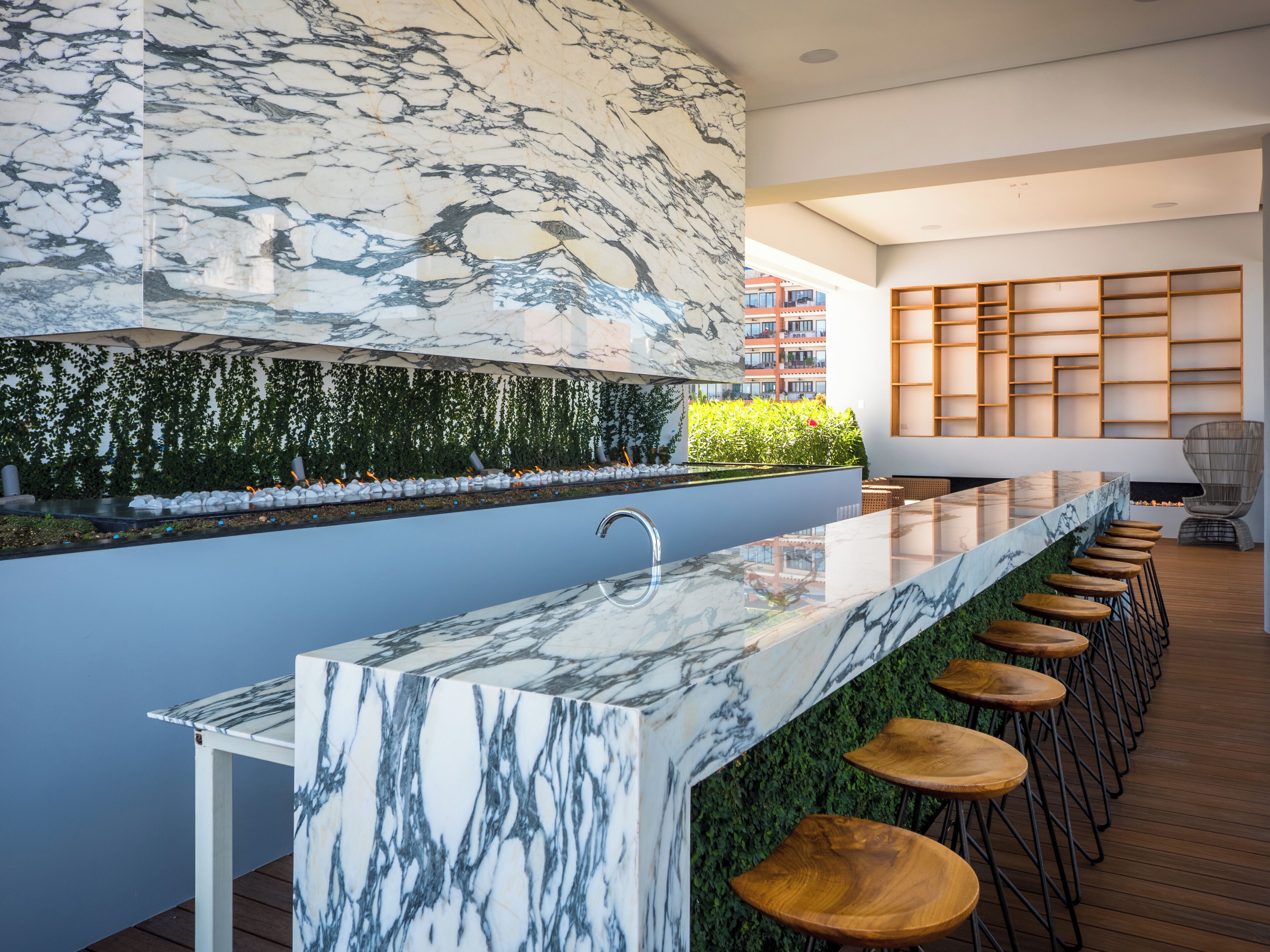 A modern kitchen with a marble countertop, bar stools, and a green wall with plants.