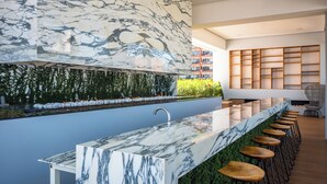 A modern kitchen with a marble countertop, bar stools, and a green wall with plants. - Ritzy Pier 57 Ocean Views Ocean Views Rooftop Pool Zona Romantica (Puerto Vallarta)