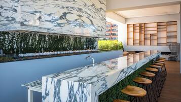 A modern kitchen with a marble countertop, bar stools, and a green wall with plants.