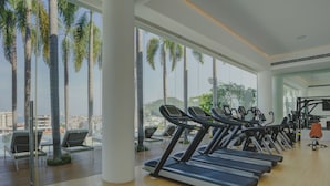 Ett gym med löpband, motionscyklar och utsikt över palmer och byggnader.
