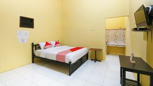 A small, yellow-walled room with a bed, a table, a TV, and a patterned curtain. - El Shaday Family Residence (Banyuwangi)