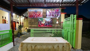 A covered outdoor area with a table and chairs, a green gate, and a wall with posters. - El Shaday Family Residence (Banyuwangi)