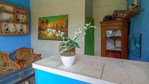 A reception area with a blue counter, a potted plant, a painting, and a wooden cabinet with folded clothes. - El Shaday Family Residence (Banyuwangi)