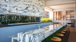 A modern kitchen with a marble countertop, bar stools, and a green wall with plants. - Ritzy Pier 57 Penthouse  Ocean Views Romantic Zone (Puerto Vallarta)