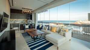 A modern living room with a large sofa, a coffee table, and a TV. There is a balcony with a view of the sea and buildings. - Ritzy Pier 57 Penthouse  Ocean Views Romantic Zone (Puerto Vallarta)