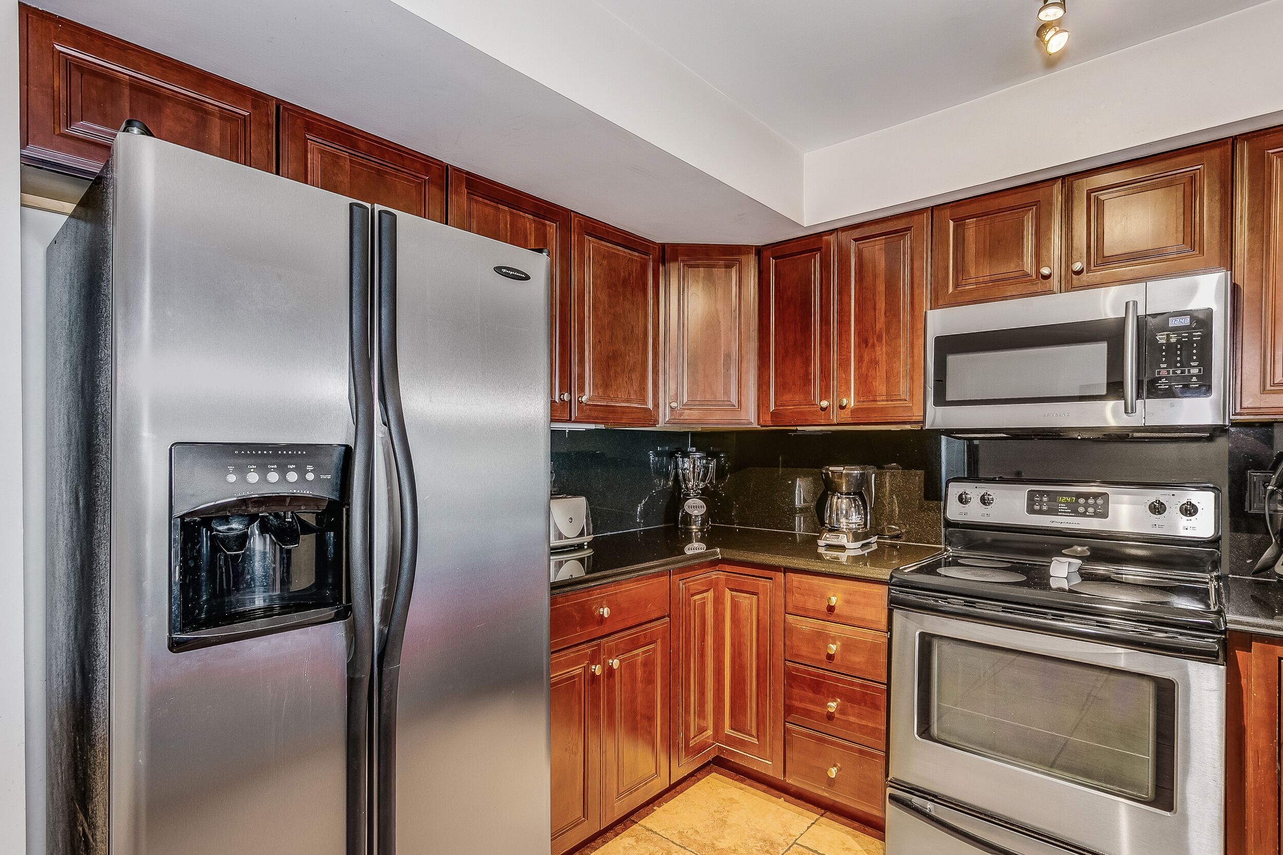 A kitchen with wooden cabinets, a stainless steel refrigerator, a microwave, and an oven.