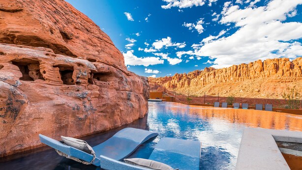 Une piscine avec des chaises longues, une falaise rocheuse et un ciel dégagé.