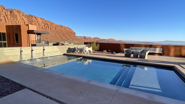 Ein Schwimmbecken mit freiem Blick auf die umliegende Landschaft, darunter ein Wüstenberg und ein modernes Gebäude mit Terrasse.