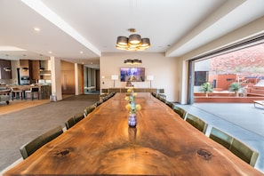 A spacious conference room with a long wooden table, surrounded by chairs, and a large window offering a view of an outdoor area with plants.