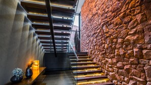 Moderni portaikko, jossa on lasikaiteet, kiviseinä ja koriste-esineillä varustettu puinen penkki.