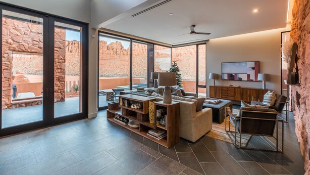 A spacious living room with a large window, a fireplace, and a stone wall. - Luxury Service 3 Kings and Bunks & PRIVATE Pool - Sleeps 12 -  Daily HK (Ivins)