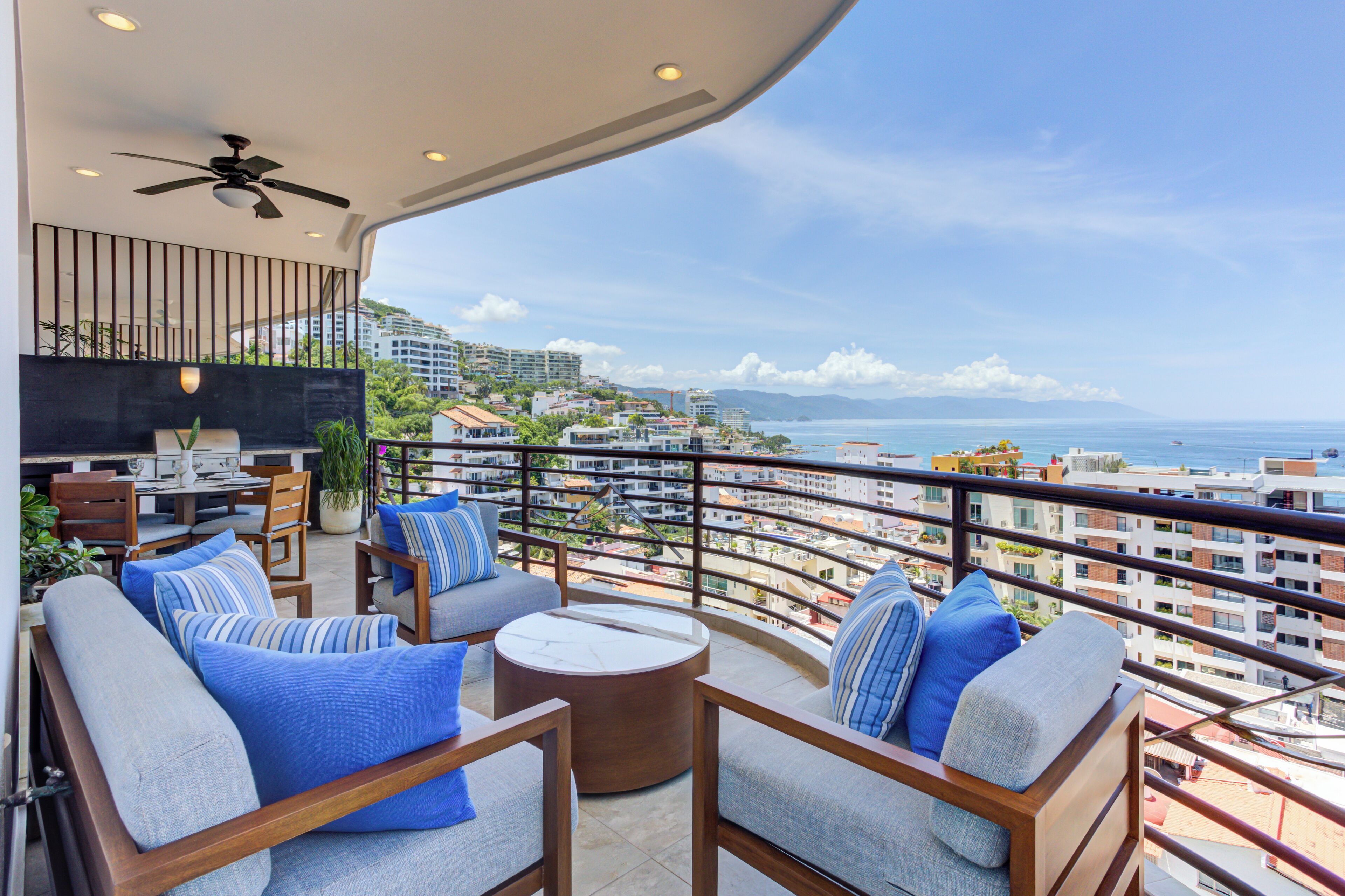 Un balcon avec coin salon extérieur, un ventilateur de plafond et une vue sur la ville et la mer.